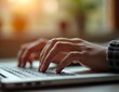© hendar - Hands of a person typing on a laptop keyboard, with a close-up focus on the hands and keyboard. The background is softly blurred, suggesting an indoor environment with natural light. The person appear