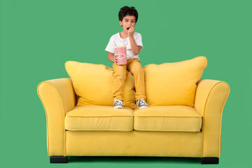 Little boy with popcorn watching movie on sofa against green background