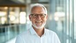 © Phirakhup - Cheerful older man in glasses smiling brightly in a modern office environment.