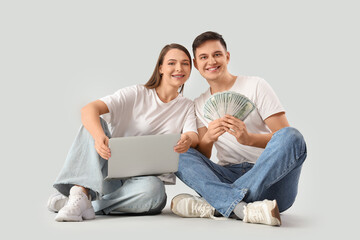 Wall Mural - Young couple with money and laptop sitting on light background