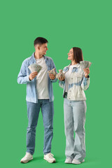 Wall Mural - Happy young couple with money and sack bags on green background