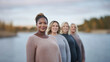 © tashechka - A group of four people standing by a calm lake, with soft natural lighting and a serene, relaxed atmosphere.