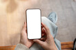 © bongkarn - A top view of a woman sits indoors and holds a smartphone with a white screen mockup.