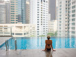© YURII Seleznov - Young asian woman relaxing by pool at Kuala Lumpur hotel with view of surrounding skyscrapers, enjoying leisure time in vibrant urban setting.