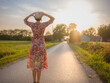 © YURII Seleznov - Young woman walking through picturesque European field in late summer. Golden sunlight, lush greenery, and serene rural atmosphere create peaceful countryside scene.