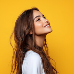 Portrait of a happy young woman with wavy hair, wearing a yellow jacket and smiling while looking up, isolated on a bright background. 
