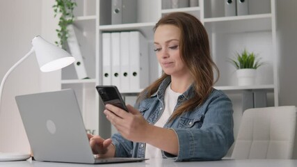 Poster - A young woman is deeply focused on her smartphone and laptop within an elegantly styled, modern office environment that successfully merges aesthetic appeal with practicality, enhancing her workflow