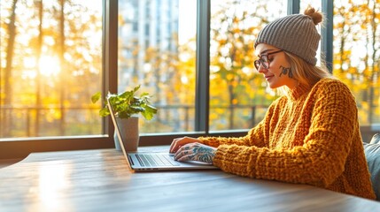 Poster - Woman sitting at a table using a laptop with a focused expression on a bright and modern workspace