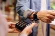 © Seventyfour - Close-up image of man's hand using smartwatch for contactless payment at a store checkout counter, demonstrating convenience and modern technology in everyday transactions