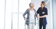 © peopleimages.com - Clinic, caregiver and balance for woman with disability, kindness or smile for support for physical therapy. Healthcare, patient and senior person with walker in nursing home, space or rehabilitation