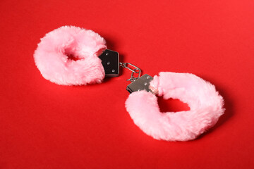 Wall Mural - Pink fluffy handcuffs on red background. Sex toy