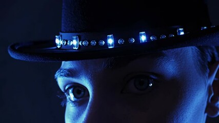 Poster - close-up of a woman's face illuminated by blue lights emanating from her fedora hat, creating a myst