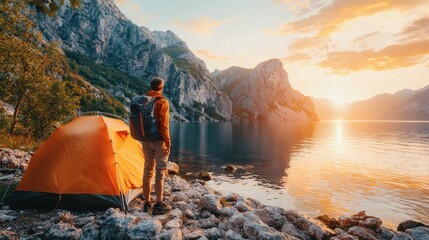 Poster - Hiker standing on a rocky shoreline near a tent watching the sunrise over the horizon peaceful morning at a coastal campsite Stock Photo with side copy space