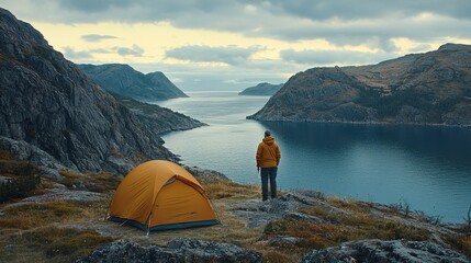 Poster - Hiker standing on a rocky shoreline near a tent watching the sunrise over the horizon peaceful morning at a coastal campsite Stock Photo with side copy space