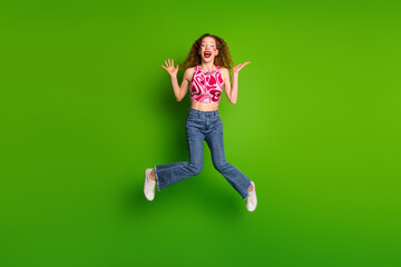 Wall Mural - Cheerful young woman jumping mid-air on a vibrant green background, radiating happiness and positivity