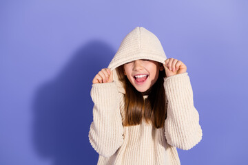 Wall Mural - Cheerful young girl wearing a cozy sweater posing against a purple background, expressing happiness and charm