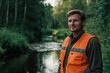 © Mediaphotos - Smiling man standing outdoors wearing orange safety vest and smiling with forested area and river background providing a serene and natural setting