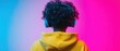 © Fernando - Back view of a young Black person with curly hair wearing blue headphones and a yellow hoodie against a vibrant pink and blue gradient background Concept of music, technology, and youth