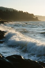 Wall Mural - Captivating view of ocean waves hitting rocks under a golden sunset, with a forested coastline in the background.