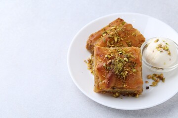 Wall Mural - Tasty baklava with chopped nuts and scoop of ice cream on light grey table, closeup. Space for text