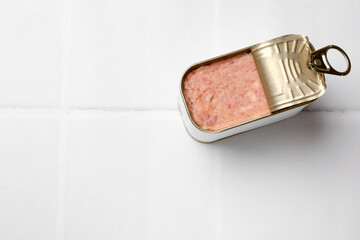 Wall Mural - Tasty canned meat in tin can on white tiled table, top view. Space for text