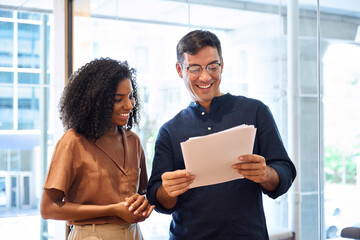 Aufkleber - Business team of two happy young busy diverse colleagues, professional business man and business woman executives working together standing in office looking at project documents and talking.