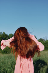 Canvas Print - Young woman with flowing red hair in a pink dress enjoying nature against a green backdrop, representing freedom and natural beauty