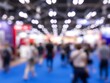 © Kowshar habib - Blurred Crowd of Anonymous People Walking on Blue Floor at Indoor Trade Show Exhibition with Bokeh Lights Abstract Background