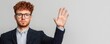© CassiOpeiaZz - A young man with curly hair and glasses raises his hand, looking serious, in a smart outfit against a neutral background.
