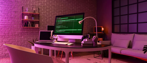 Wall Mural - Programmer's workplace with computer, laptop and glowing lamp in dark office