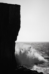 Wall Mural - a black and white photo of a cliff overlooking the ocean. the water is choppy and the waves are cras