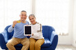 © artitwpd - Happy Asian senior couple looking at the camera and showing credit card and tablet while sitting on a sofa in the living room. Senior adults using online banking and technology. Image with copy space.