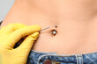 © Pixel-Shot - Professional doing piercing of young woman's navel on grey background, closeup
