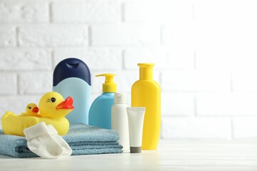 Wall Mural - Baby cosmetic products, socks, towel and rubber ducks on table against white brick wall. Space for text