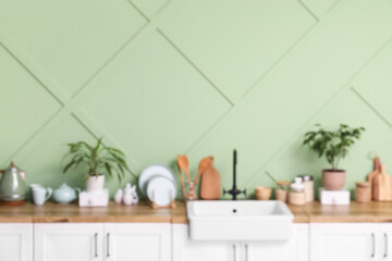 Canvas Print - Blurred view of modern kitchen with counters, sink and utensils near green wall