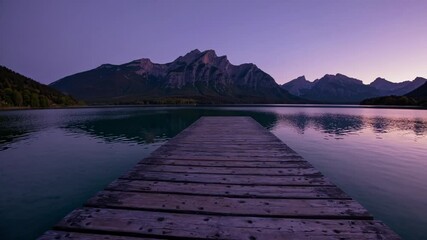 Poster - A quaint wooden pier extending into a glassy lake at twilight, with purple-hued mountains reflecting in the still water.
