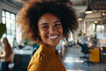 Wall Mural - woman with curly hair is smiling in a room with a yellow chair. The room has a business setting with a few other people in the background