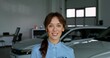 © m-art - A woman in formal clothes smiles standing among the cars in the showroom. Car Dealership Manager