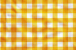 © A.Ex - Yellow and white checkered fabric draped elegantly over a rustic wooden table, creating a vibrant and cozy look.