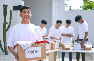 Portrait Of Young Teenage Boy Showing Clothes Donation Box Against Community Working Together Background 