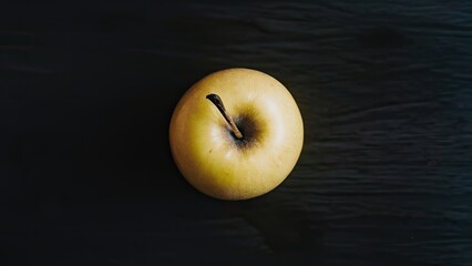 Poster - A golden yellow apple centered on a dark wooden backdrop, with a soft light illuminating its surface for a vibrant contrast.