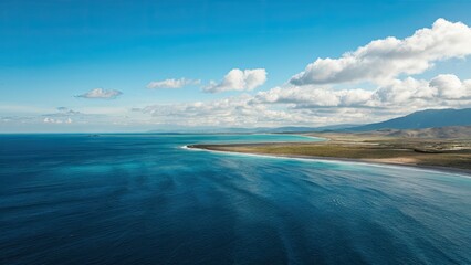 Poster - Expansive blue ocean waters under a clear sky with soft clouds, featuring a flat coastal landscape and gentle waves reflecting turquoise hues.