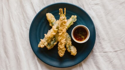 Poster - Tempura vegetables arranged in a cross pattern on a dark blue plate with a small dish of ponzu sauce over a light textured background