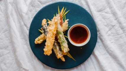 Poster - Tempura vegetables arranged on a teal plate with a small bowl of dark ponzu sauce positioned to the right on a white textured background.