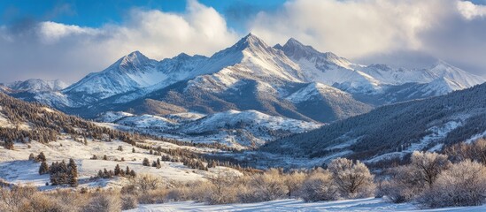 Wall Mural - Majestic snow-covered mountain range under a blue sky with fluffy clouds showcases serene winter landscape and frosted trees in foreground