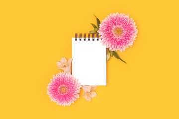Wall Mural - clean notepad mockup. frame made of green leaves, alstroemeria and pink gerbera flowers on a yellow 