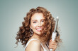 © artmim - Laughing brown haired woman with shiny long curly hairstyle showing curling iron. Hair treatment, hair care and styling