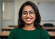 © ProArt Studios - Confident and Beautiful Indian Woman in Green Sweater and Spectacles, Smiling Brightly in Classroom or Office Setting