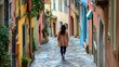 © ABC IMAGE - A woman walking down a narrow street in a European town, with cobblestones beneath her feet and colorful buildings around her
