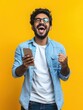 © Johannes - Excited happy young indian man winner feeling joy using smartphone winning lottery game, betting, getting cashback online gift in mobile app message holding cell phone isolated on yellow background.